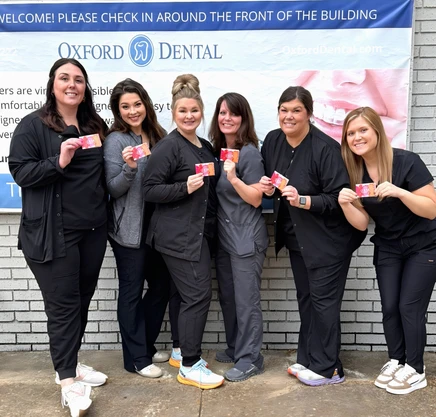 Oxford Dental team members posing together outside building, wearing pink ribbons for awareness.