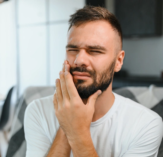 Man with hand to face experiencing tooth pain in modern home setting